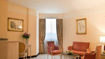 Habitación de hotel con sofá, dos sillones, una mesita, un florero con flores y dos cuadros en las paredes.