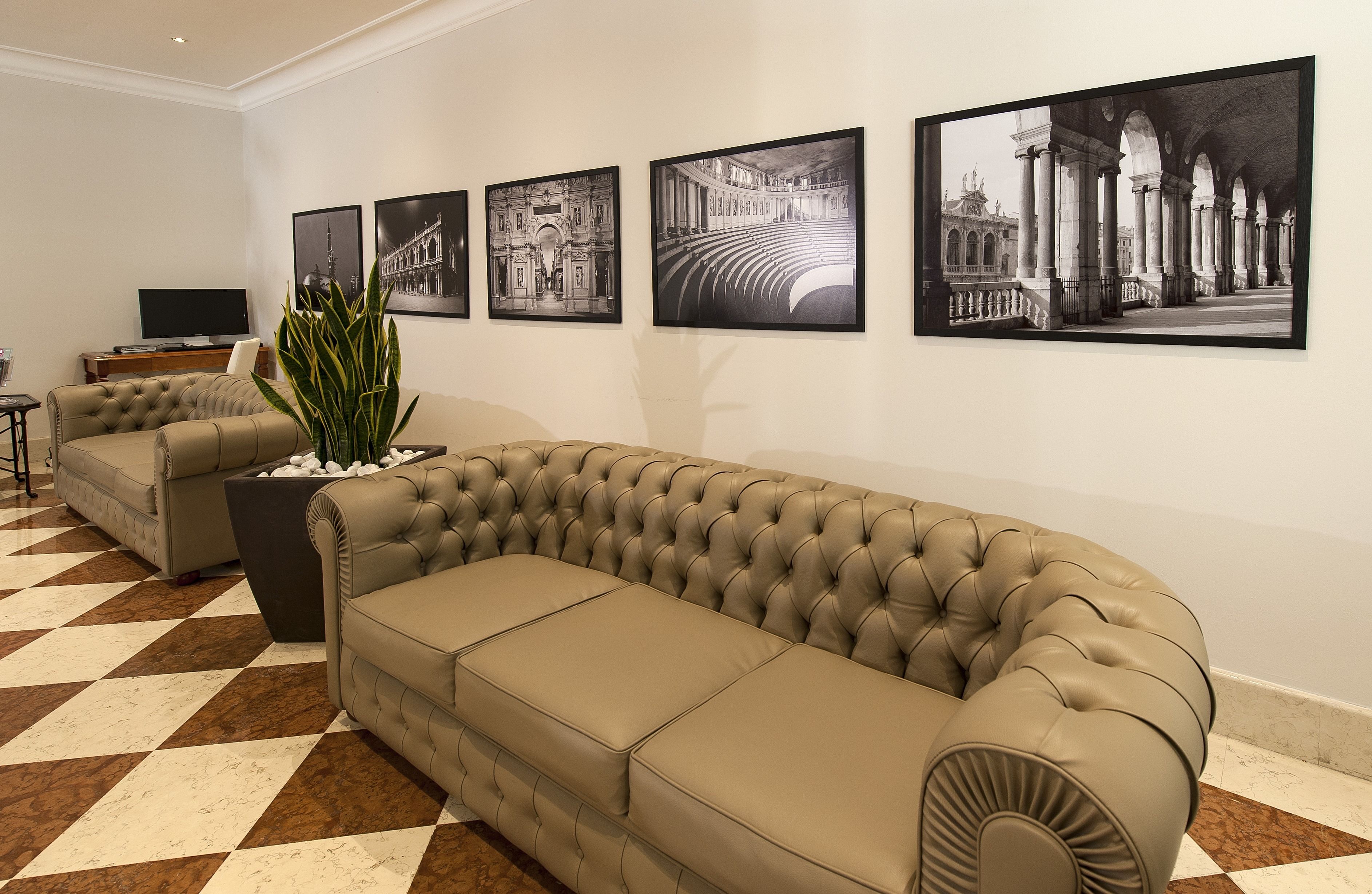 Ein modernes Wohnzimmer mit einem großen, beige gestreiften Sofa, einem kleineren Sofa und einem Couchtisch. An der Wand hängen vier schwarz-weiße Fotografien.