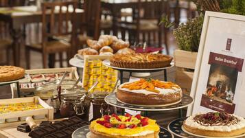 Variedad de postres y pasteles expuestos, incluyendo pasteles, tartas y hojarascas, con un cartel que indica opción de desayuno italiano.