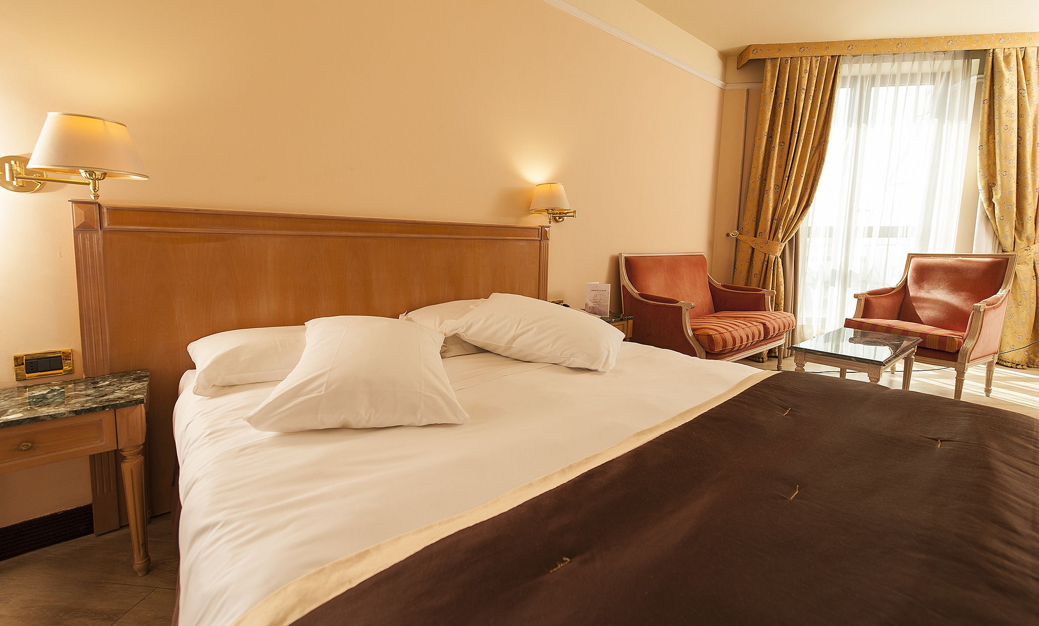 A hotel room with a large bed, two chairs, a nightstand, and a lamp.