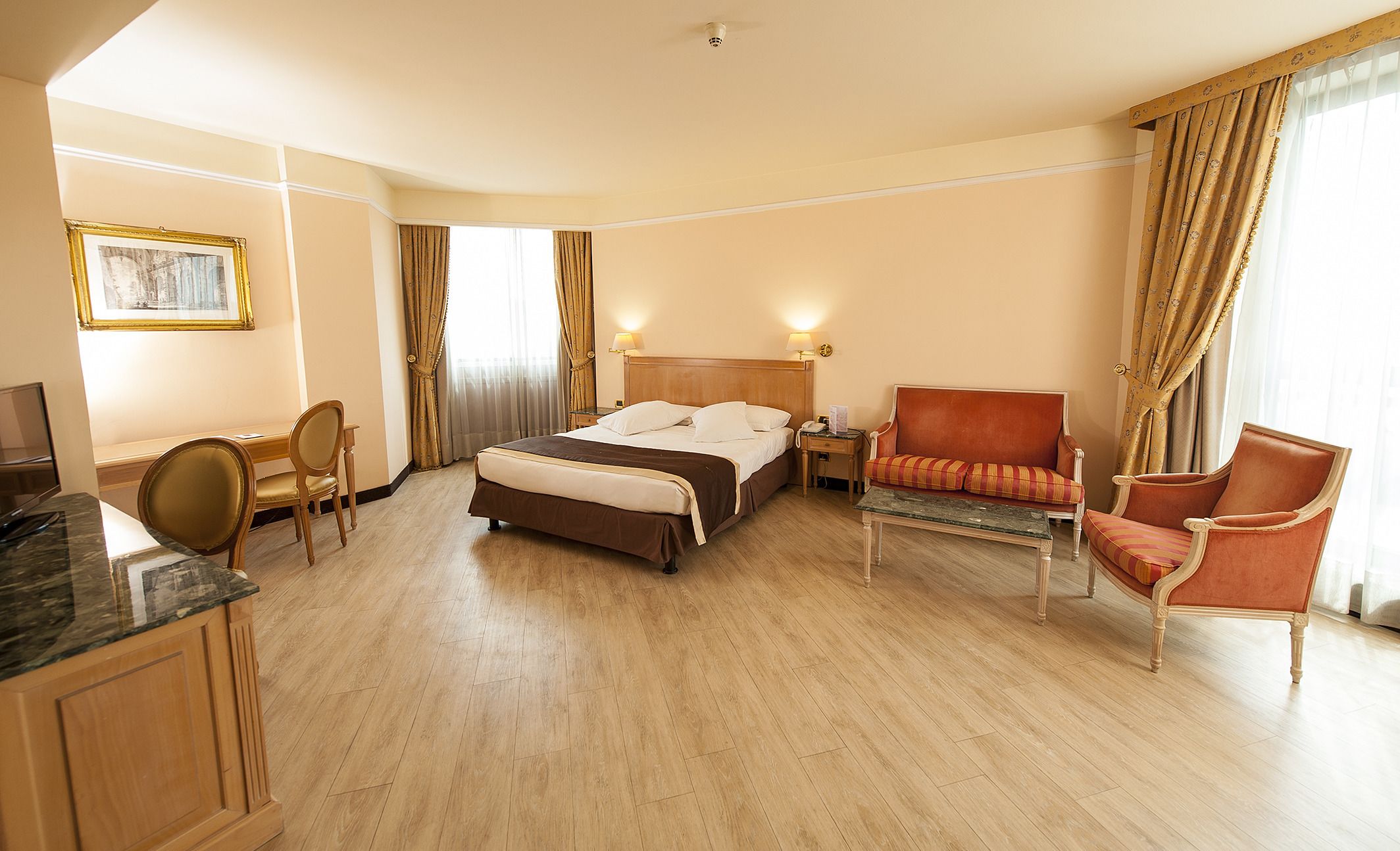 A hotel room with a bed, a desk, a chair, a sofa, and a television.