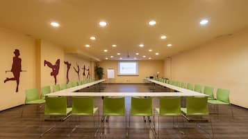 A conference room with a long table, green chairs, a projector screen, and a whiteboard.