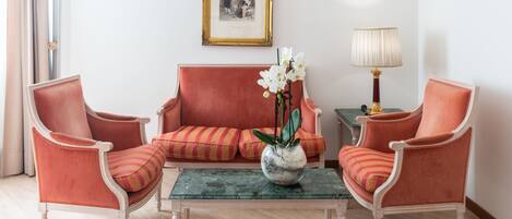 A room with a red sofa, two matching armchairs, a small table with a vase of flowers, a lamp, and a framed picture on the wall.