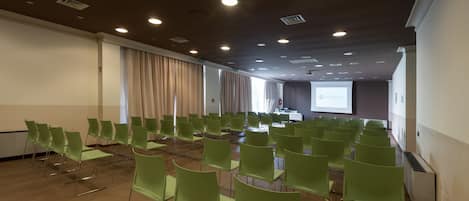 A conference room with rows of green chairs, a projector screen, and a whiteboard.