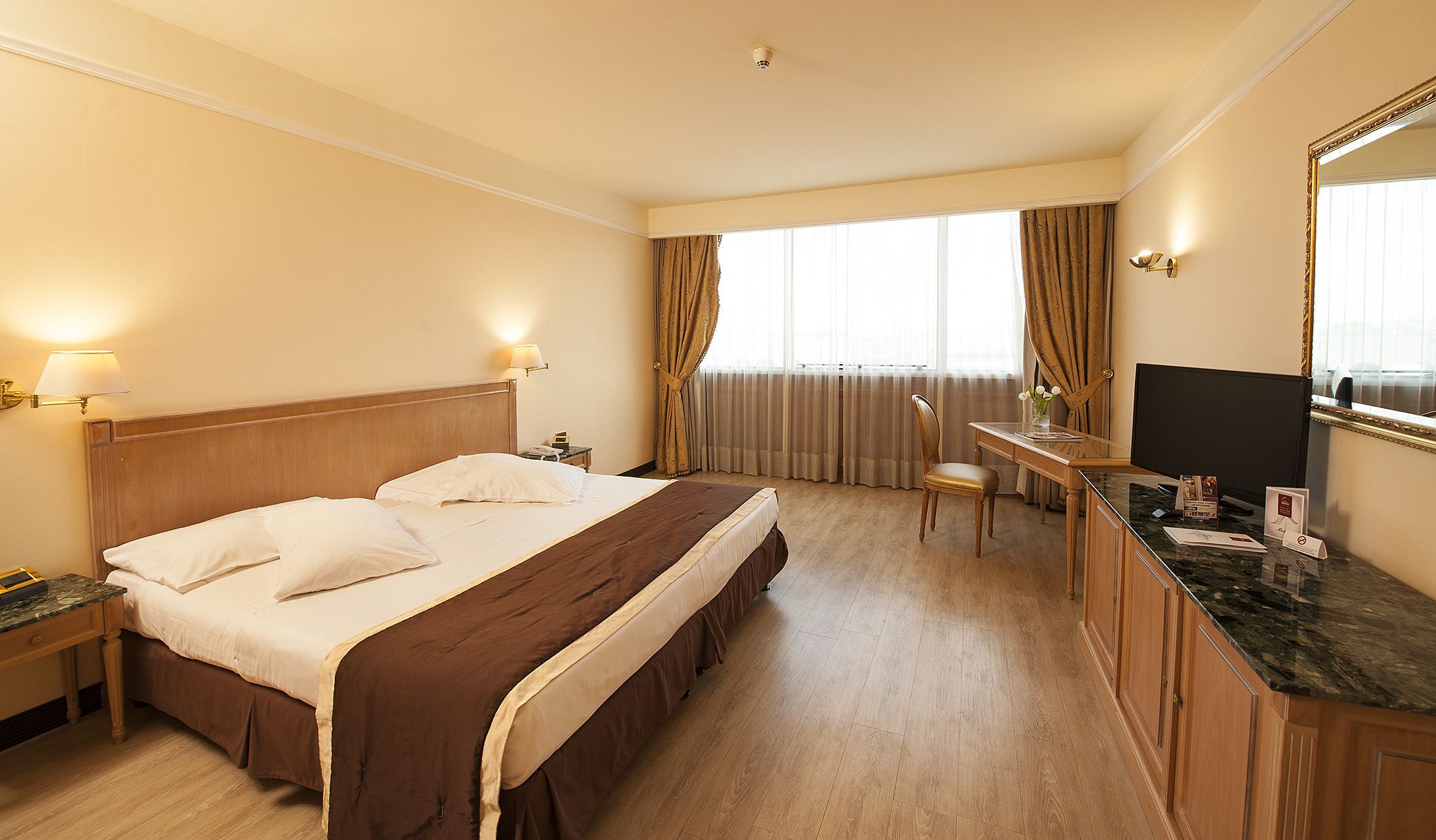 Una camera d'hotel con un letto grande, una scrivania con una sedia, una televisione e una finestra con tende.
