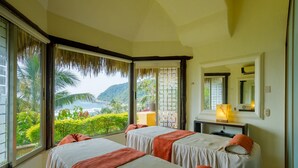 Quarto com duas camas, uma escrivaninha e uma janela grande com vista para vegetação e colinas.