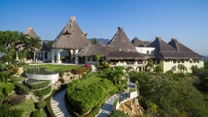 Um resort com várias construções de telhado de palha, um edifício central com um amplo pátio e um jardim bem cuidado com um caminho sinuoso.