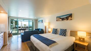 A modern hotel room with a large bed, a seating area with a sofa and chairs, and a view of the outdoors through large windows.