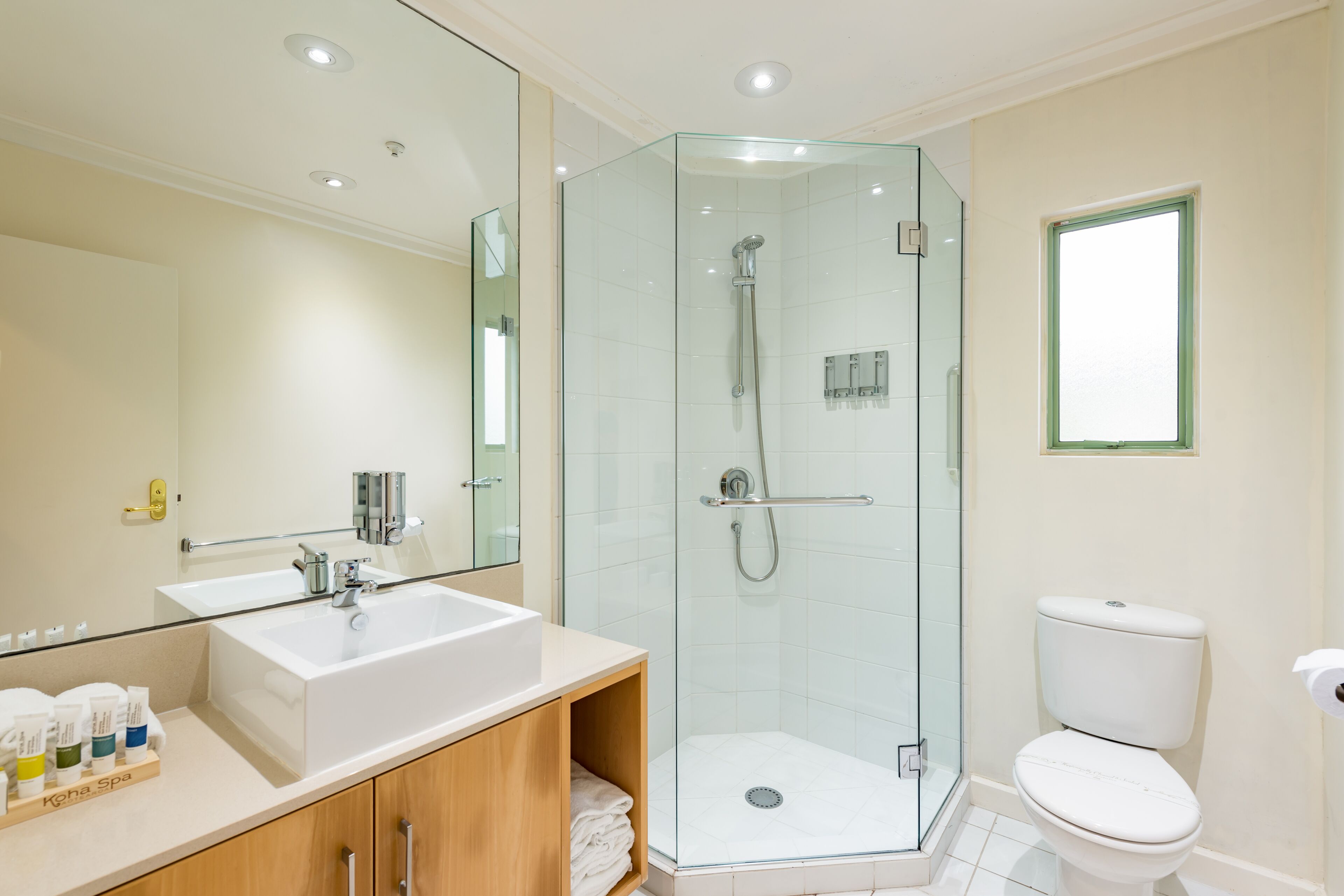 A modern bathroom with a glass-enclosed shower, a large mirror, and a white toilet.