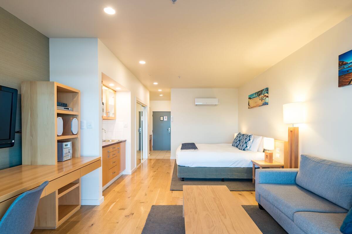 A modern hotel room with a wooden desk, a bed, a sofa, and a TV.
