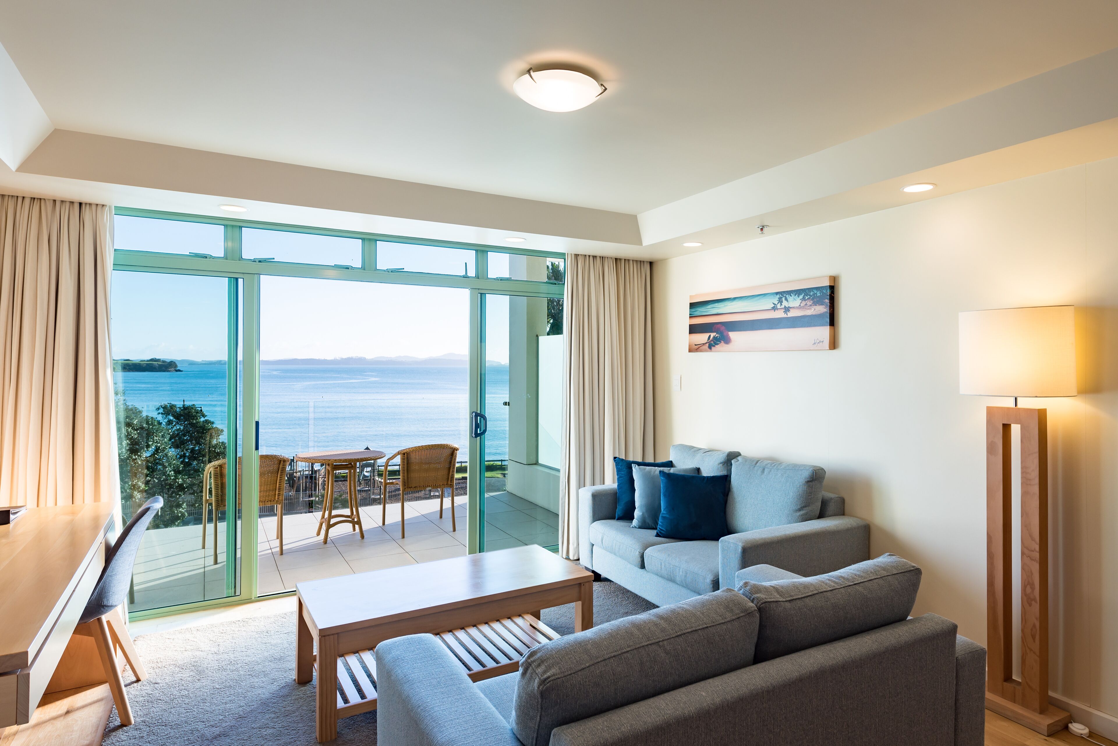 A modern living room with a sofa, a coffee table, and a view of the sea through large glass doors.