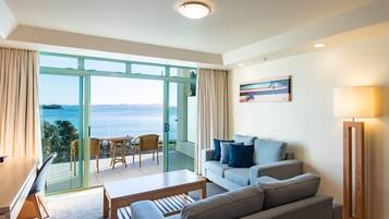 A modern living room with a sofa, a coffee table, and a view of the sea through large glass doors.
