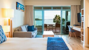 Een hotelkamer met een bed, een slaapbank, een bureau en een balkon met uitzicht op zee.