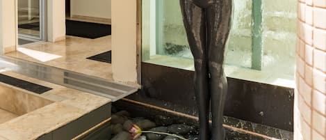 A statue in a water feature with a glass door and a tiled wall in the background.