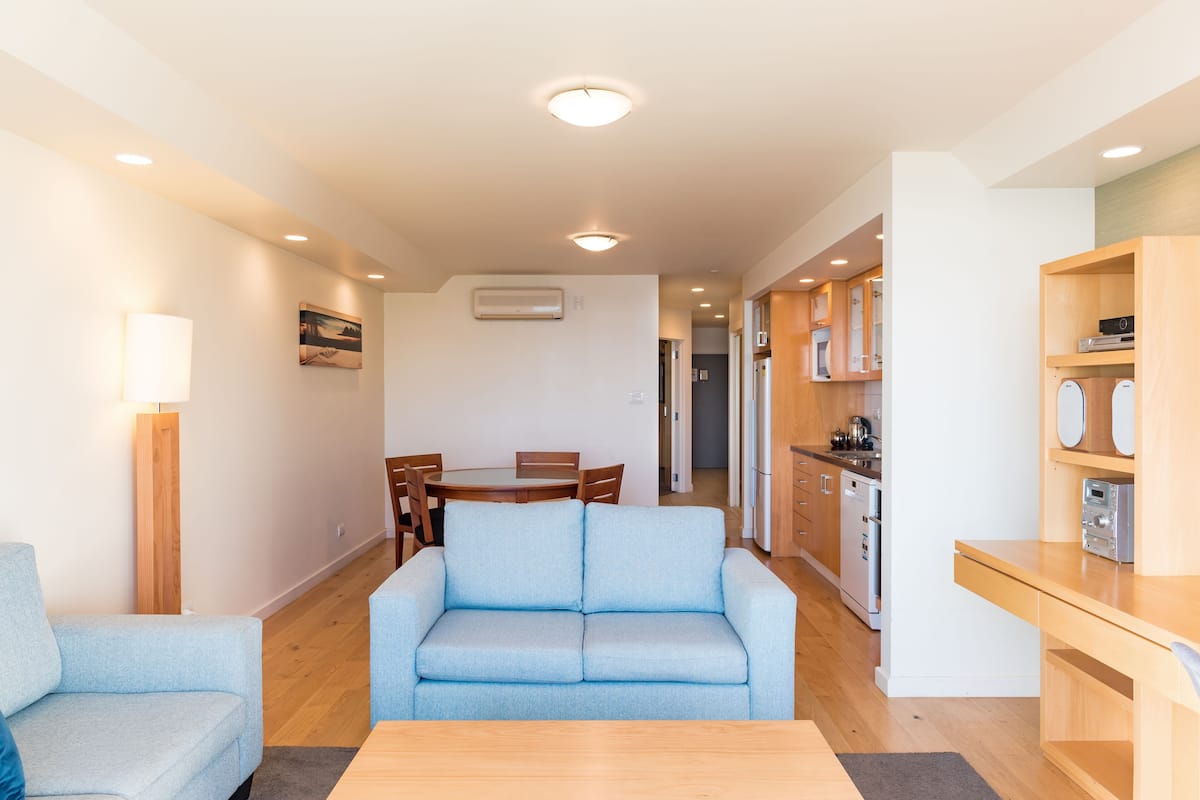 A modern living room with a sofa, a dining table, and a kitchen area.