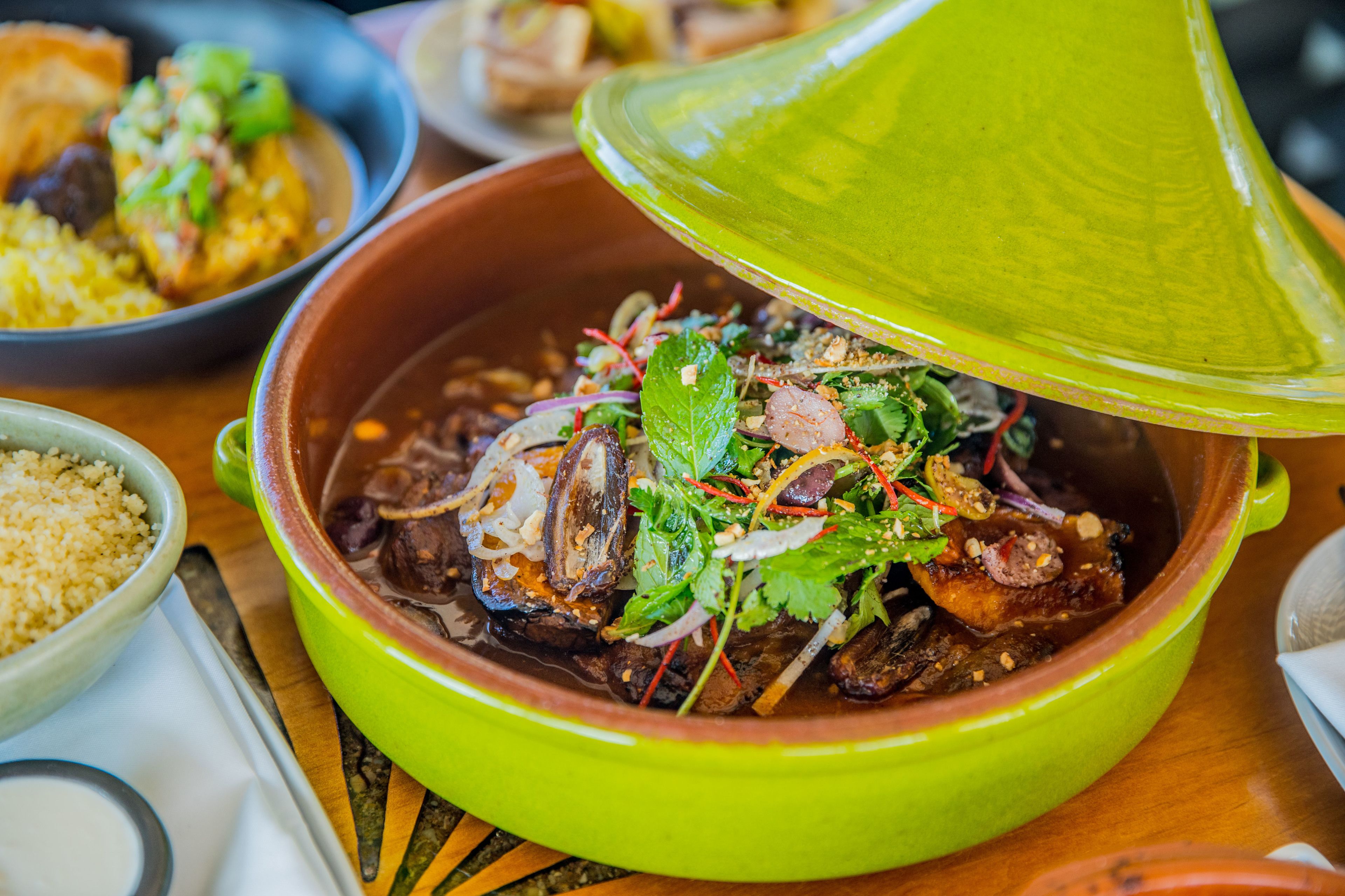 A traditional Moroccan tagine dish with a lid, surrounded by other dishes and a small bowl of couscous.