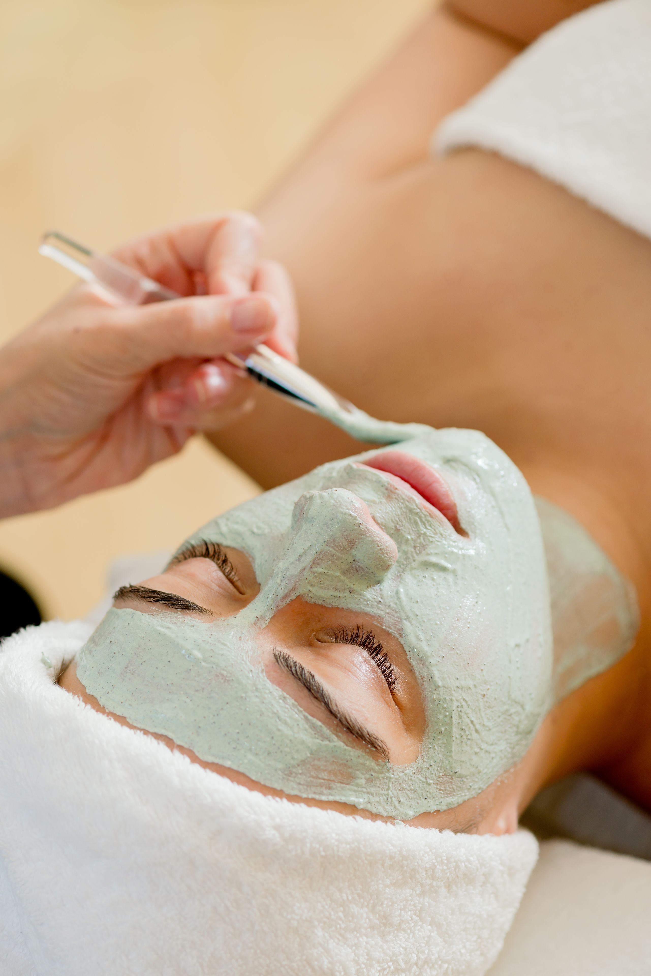 Una persona recibiendo un tratamiento facial con una mascarilla verde.
