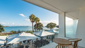 Een balkon met zitgelegenheid, uitzicht op zee en palmbomen.