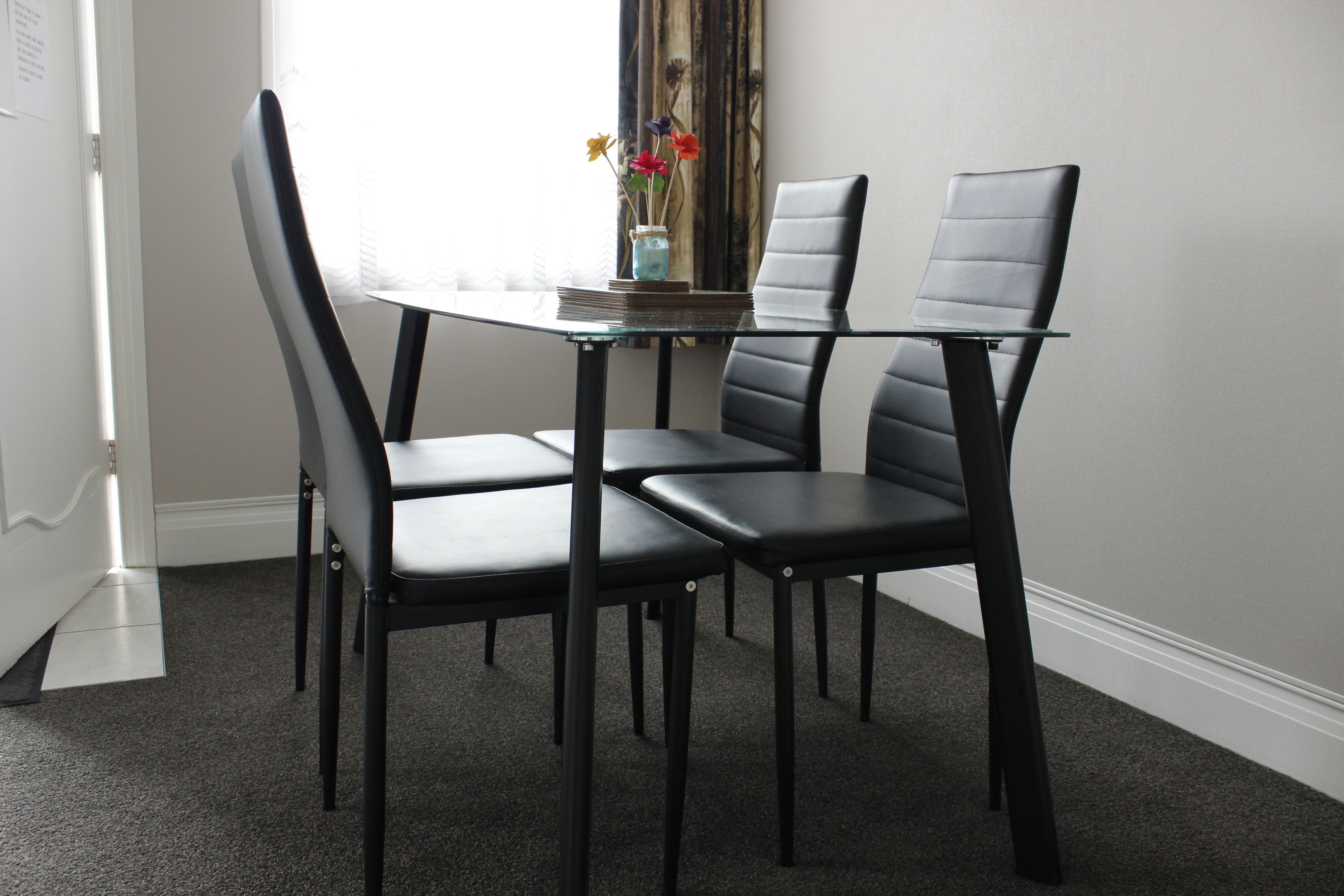 Un comedor con una mesa de vidrio y cuatro sillas negras.