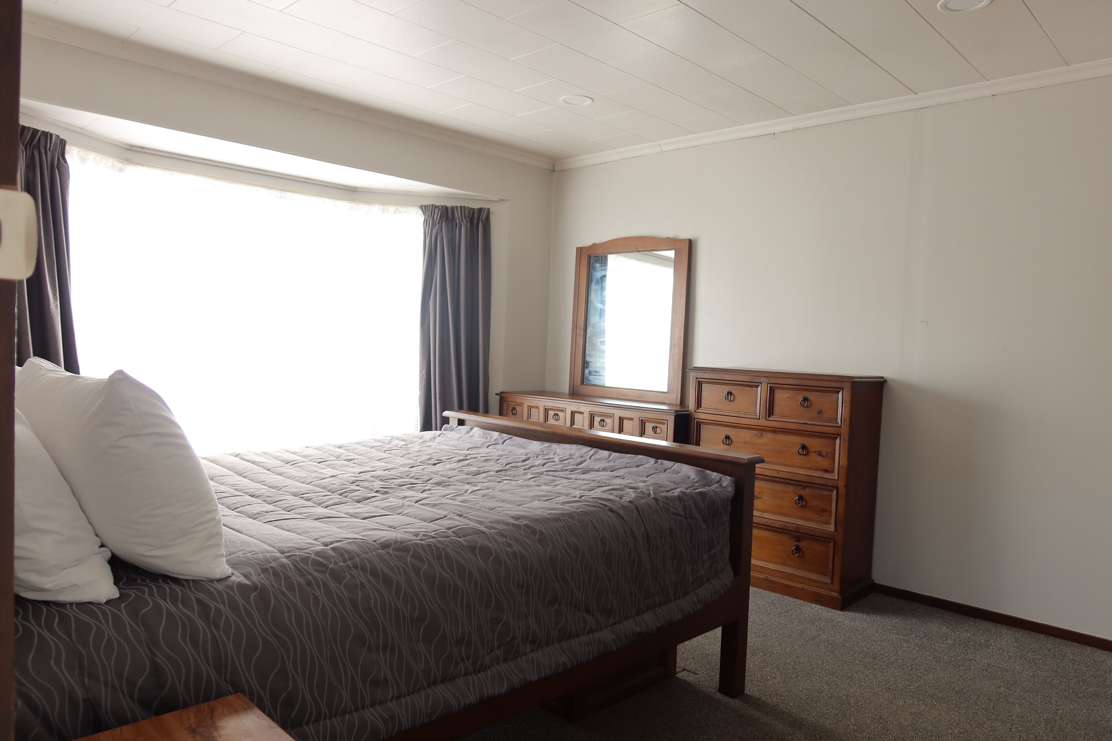 Een slaapkamer met een bed, een dressoir, een spiegel en een raam met gordijnen.