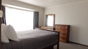 Un dormitorio con cama, cómoda, espejo y ventana con cortinas.
