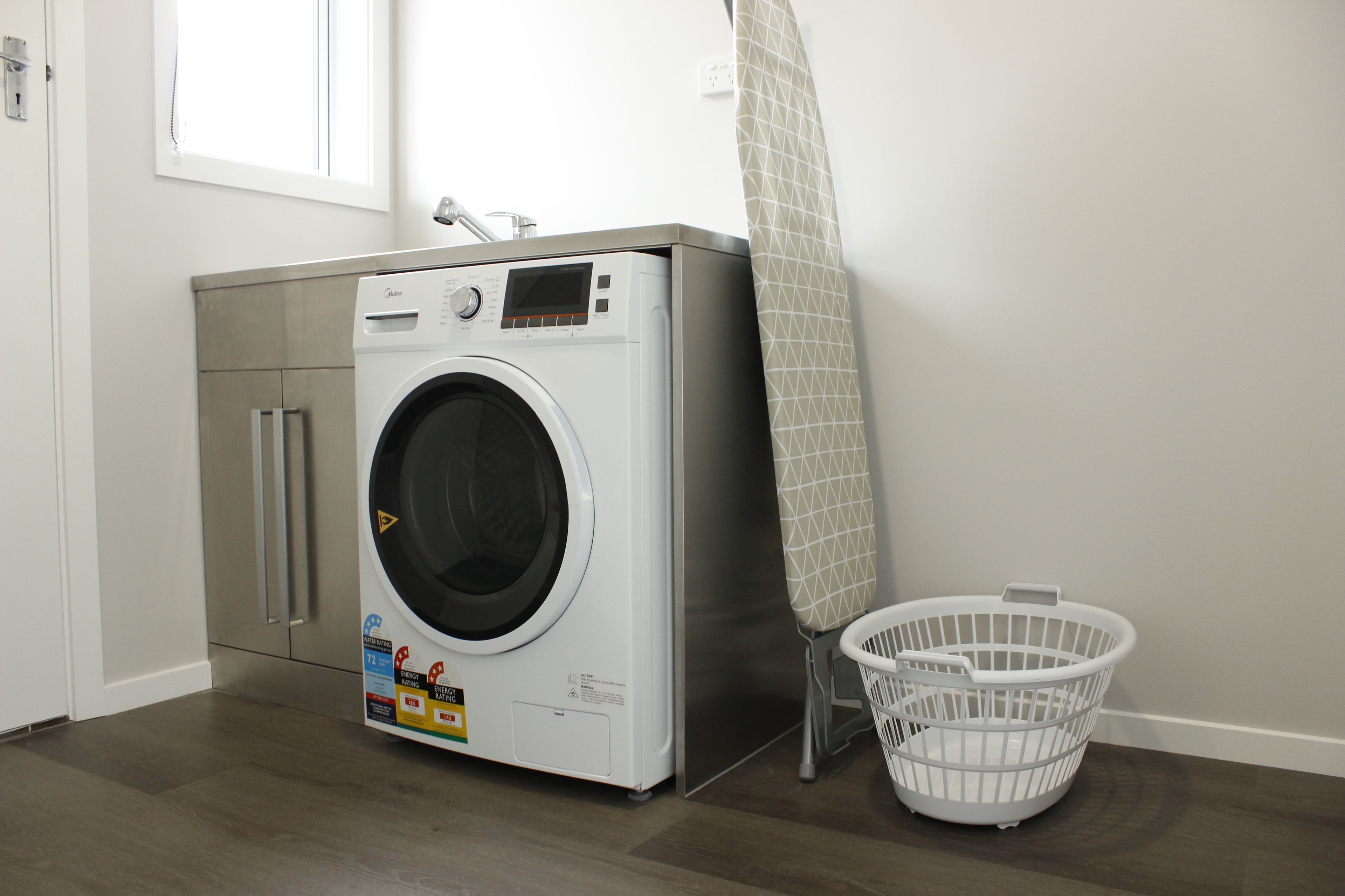 Uma  área de lavanderia com máquina de lavar, secadora e cesto de roupa branco.