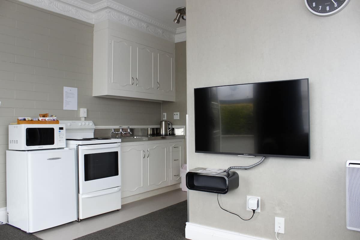 A kitchen with white appliances, a flat-screen TV mounted on the wall, and a clock on the wall.
