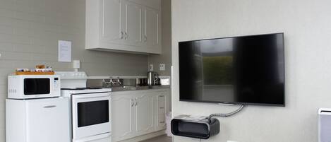 A kitchen with white appliances, a flat-screen TV mounted on the wall, and a clock on the wall.