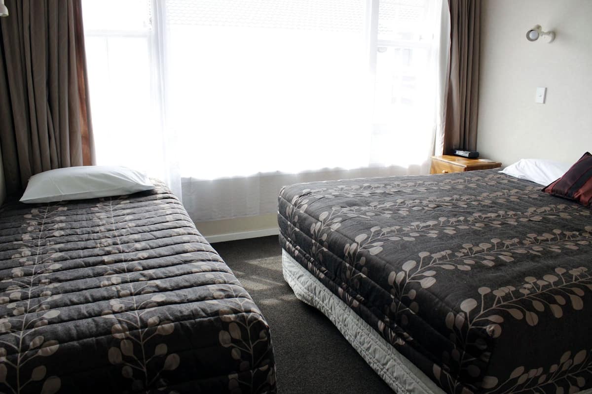 A hotel room with two beds, a nightstand, a lamp, and a window with curtains.
