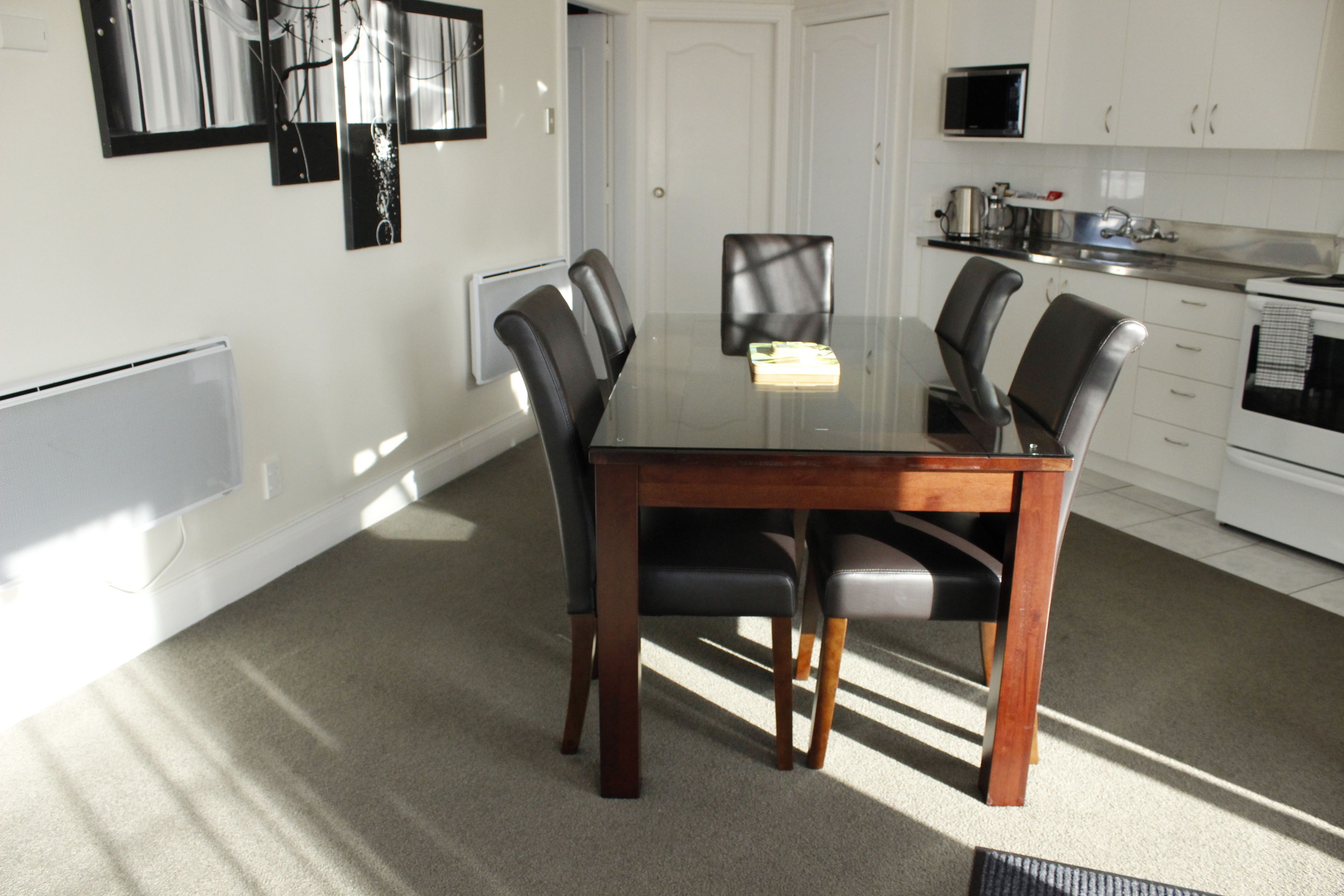 A dining area with a glass table, four chairs, and a white door in the background.