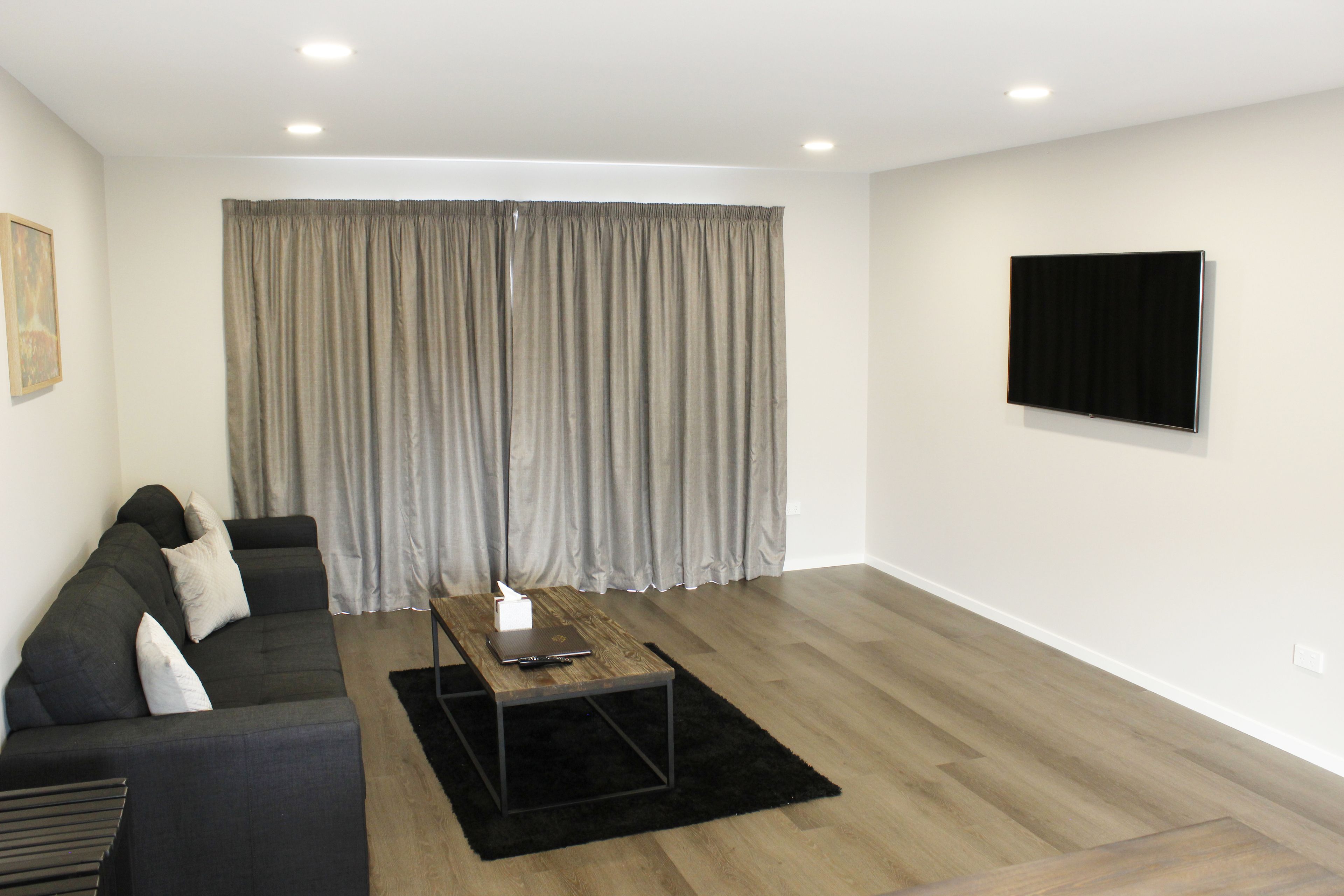 A modern living room with a dark-colored sofa, a wooden coffee table, and a large window with grey curtains.