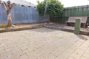 A paved patio area with a wooden bench and a tree.
