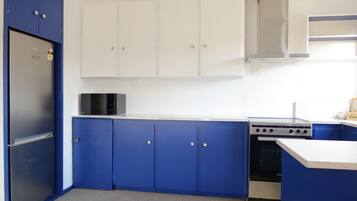 Une cuisine avec des armoires bleues, un réfrigérateur noir, un four à micro-ondes et une cuisinière.