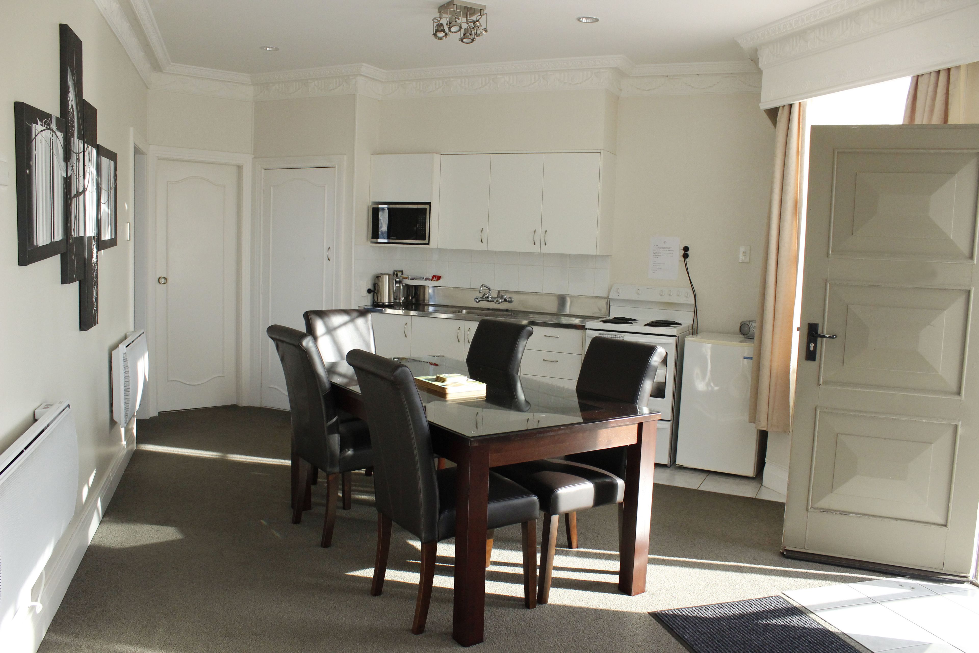 A compact kitchen with white cabinets, a microwave, and a stove. There is a dining table with four chairs.