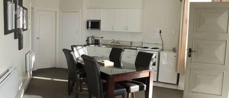 A compact kitchen with white cabinets, a microwave, and a stove. There is a dining table with four chairs.