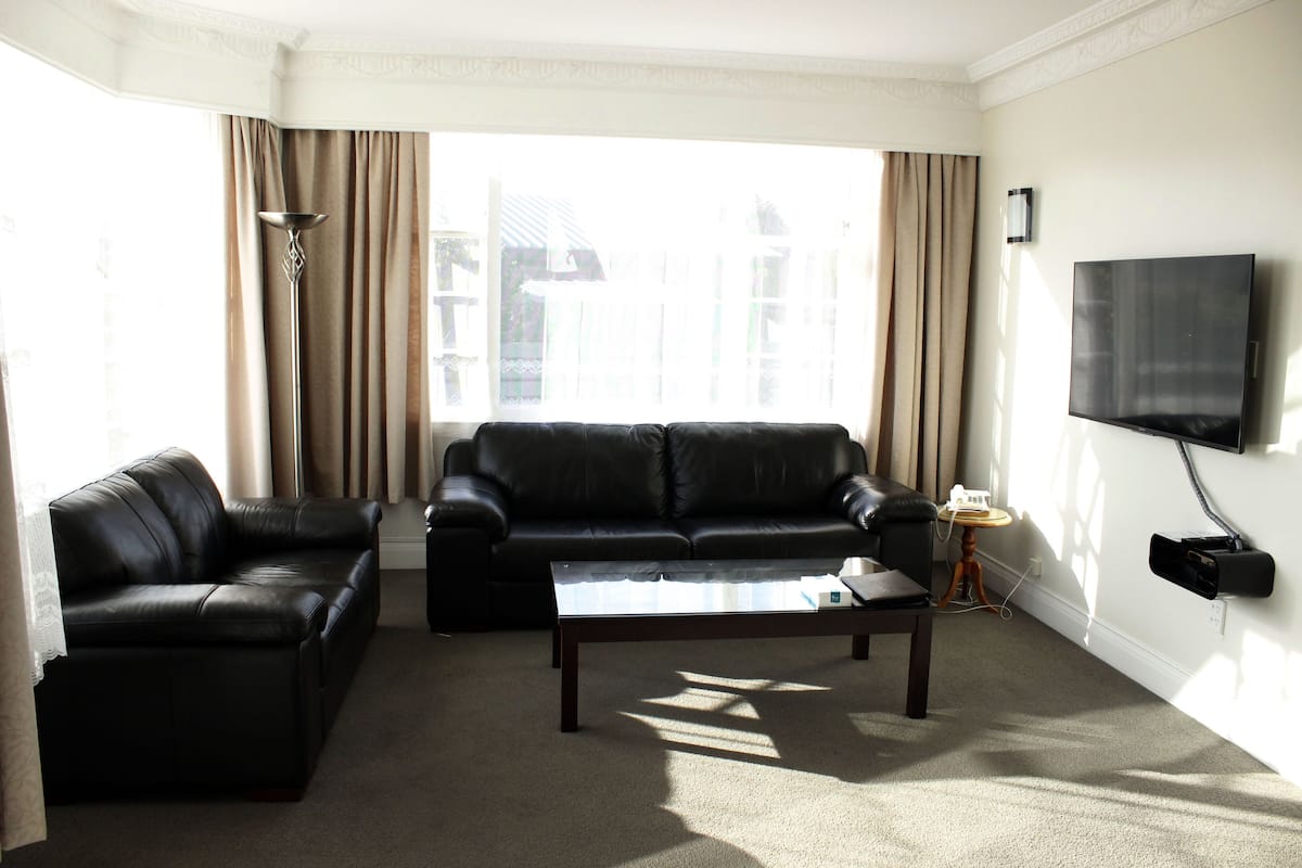 A living room with a black leather sofa, a coffee table, and a TV mounted on the wall.