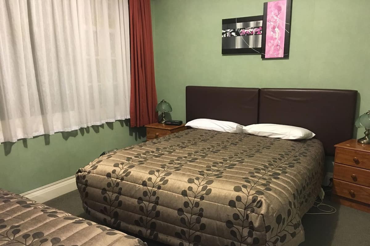 A bedroom with a bed, two bedside tables, a nightstand, a lamp, a window with curtains, and a wall art piece.