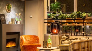 A cozy lounge area with a fireplace, comfortable seating, and a view of a balcony with plants. - Home Hotel Grand Bodø (Bodo)
