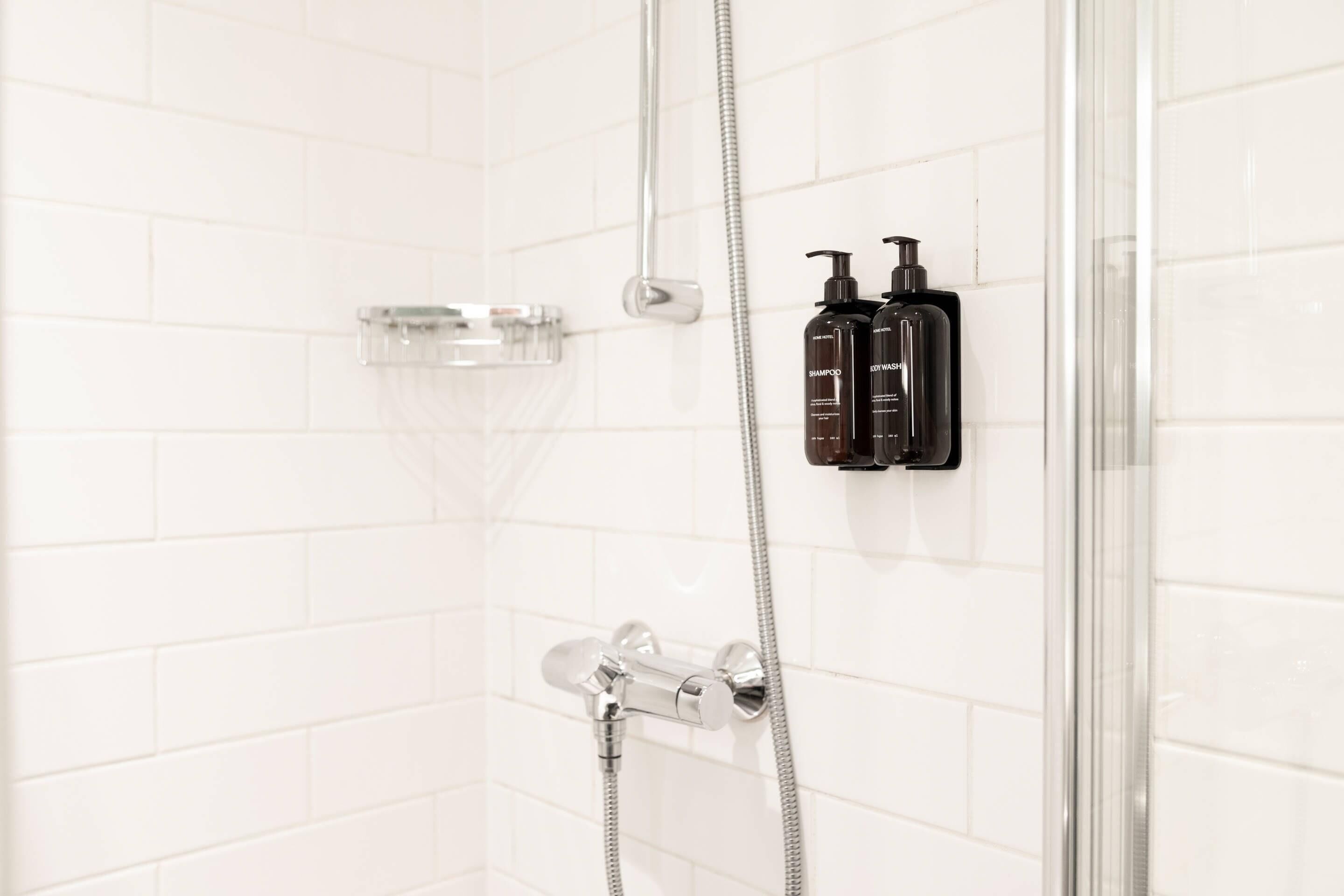 A shower area with a glass enclosure, a handheld showerhead, and two black shampoo bottles.