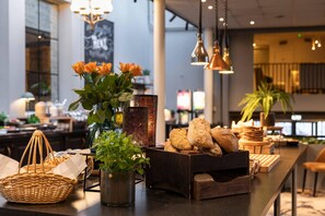 Un espace intérieur bien éclairé, avec un long comptoir où sont exposés des pains, un vase rempli de fleurs et une lampe décorative.
