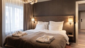 A hotel room with a large bed, two bedside lamps, a chandelier, and a view of the hallway. - Home Hotel Grand Bodø (Bodo)