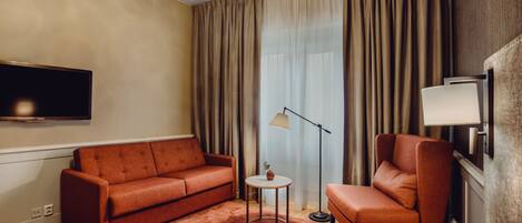 Una habitación de hotel moderna con sofá, sillón, lámpara de pie y televisor de pantalla plana.