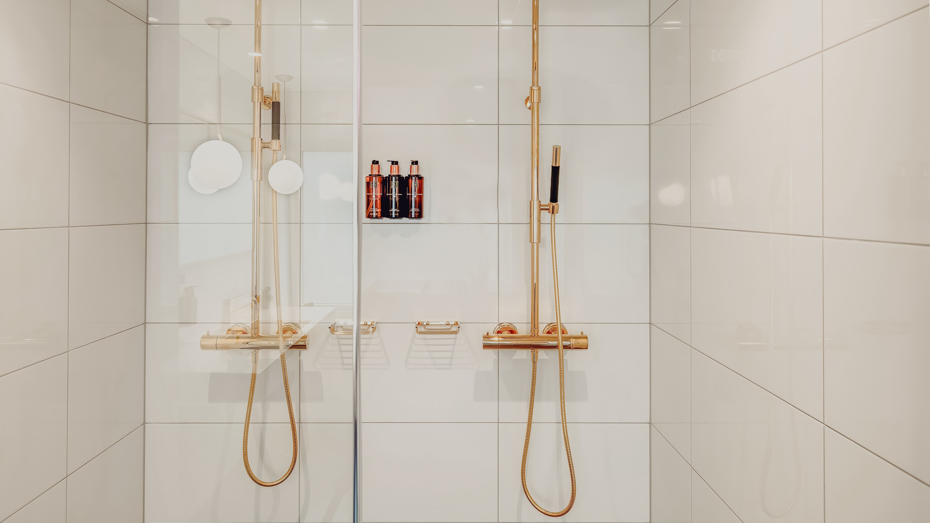 Een moderne douche met gouden details en een betegelde wand.