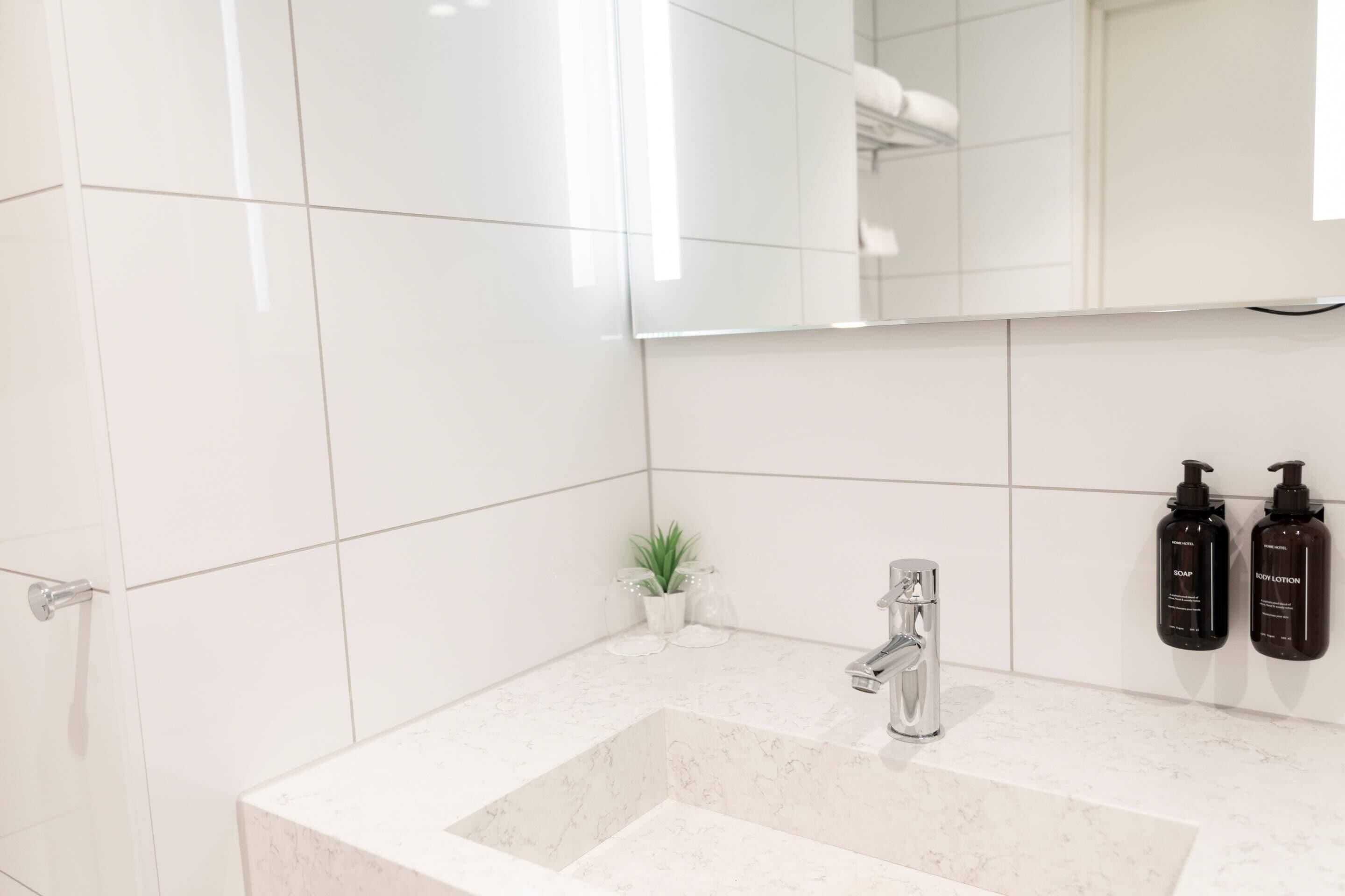 Un baño moderno con un lavamanos de mármol blanco, un espejo y dos botellas de champú y loción en la pared.