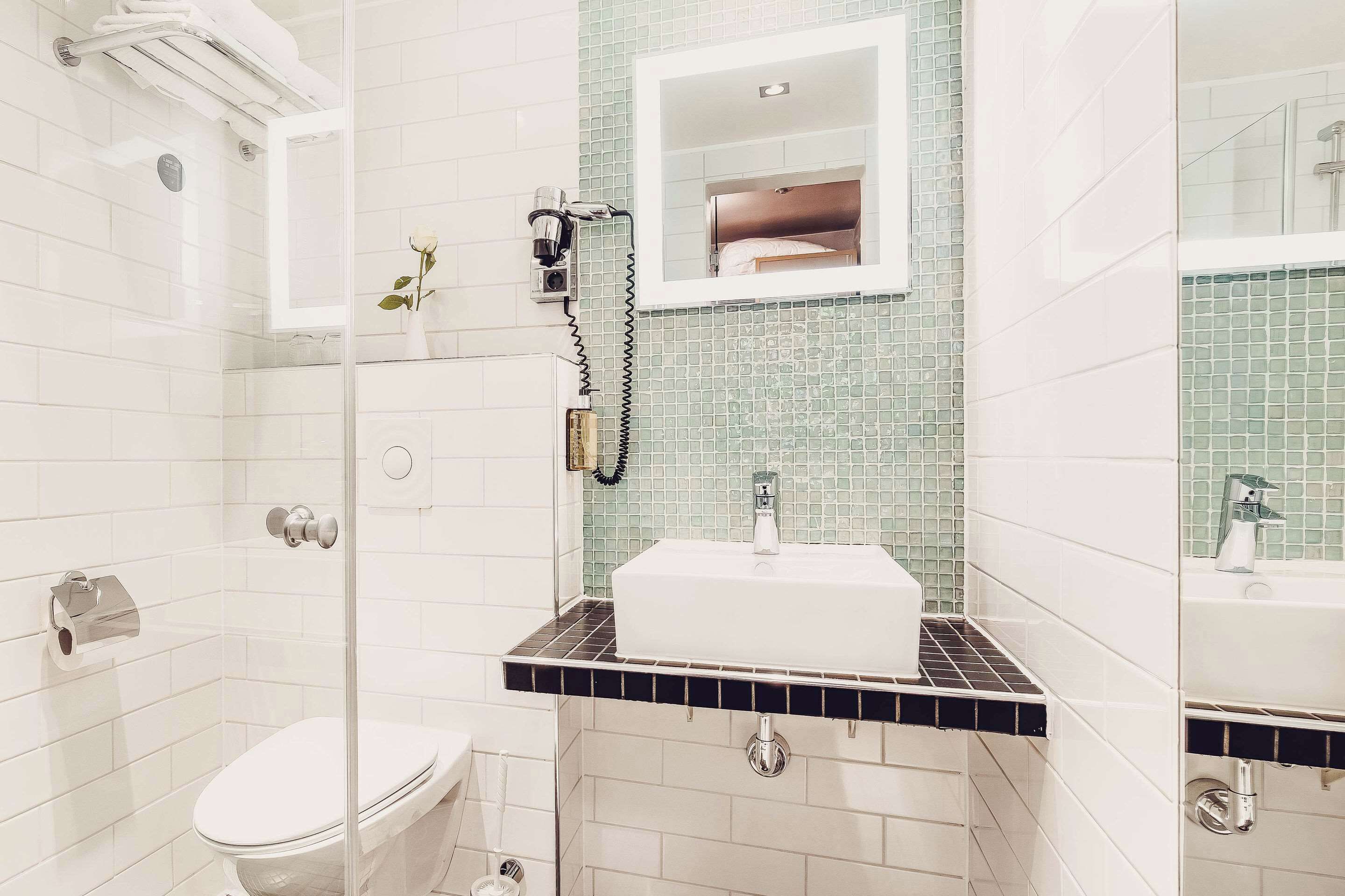 Ein Badezimmer mit Duschkabine aus Glas, einer weißen Toilette, einem Waschbecken mit schwarzer Arbeitsplatte und einem Spiegel über dem Waschbecken.