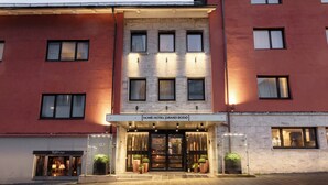 A hotel entrance with a sign reading 'Home Hotel Grand Bodo,' featuring a glass facade, multiple windows, and potted plants at the entrance. - Home Hotel Grand Bodø (Bodo)