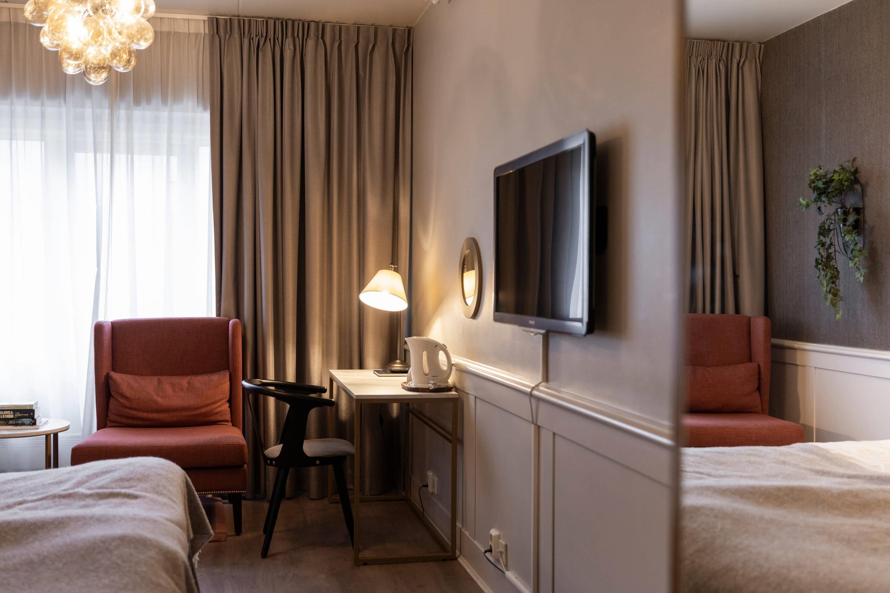 Ein Hotelzimmer mit zwei Betten, einem Schreibtisch mit Lampe, einem Fernseher und einer Pflanze.