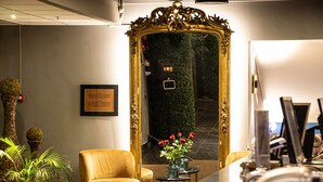 A lobby with a large mirror, two armchairs, a small table with a vase of flowers, and a framed notice on the wall. - Home Hotel Grand Bodø (Bodo)