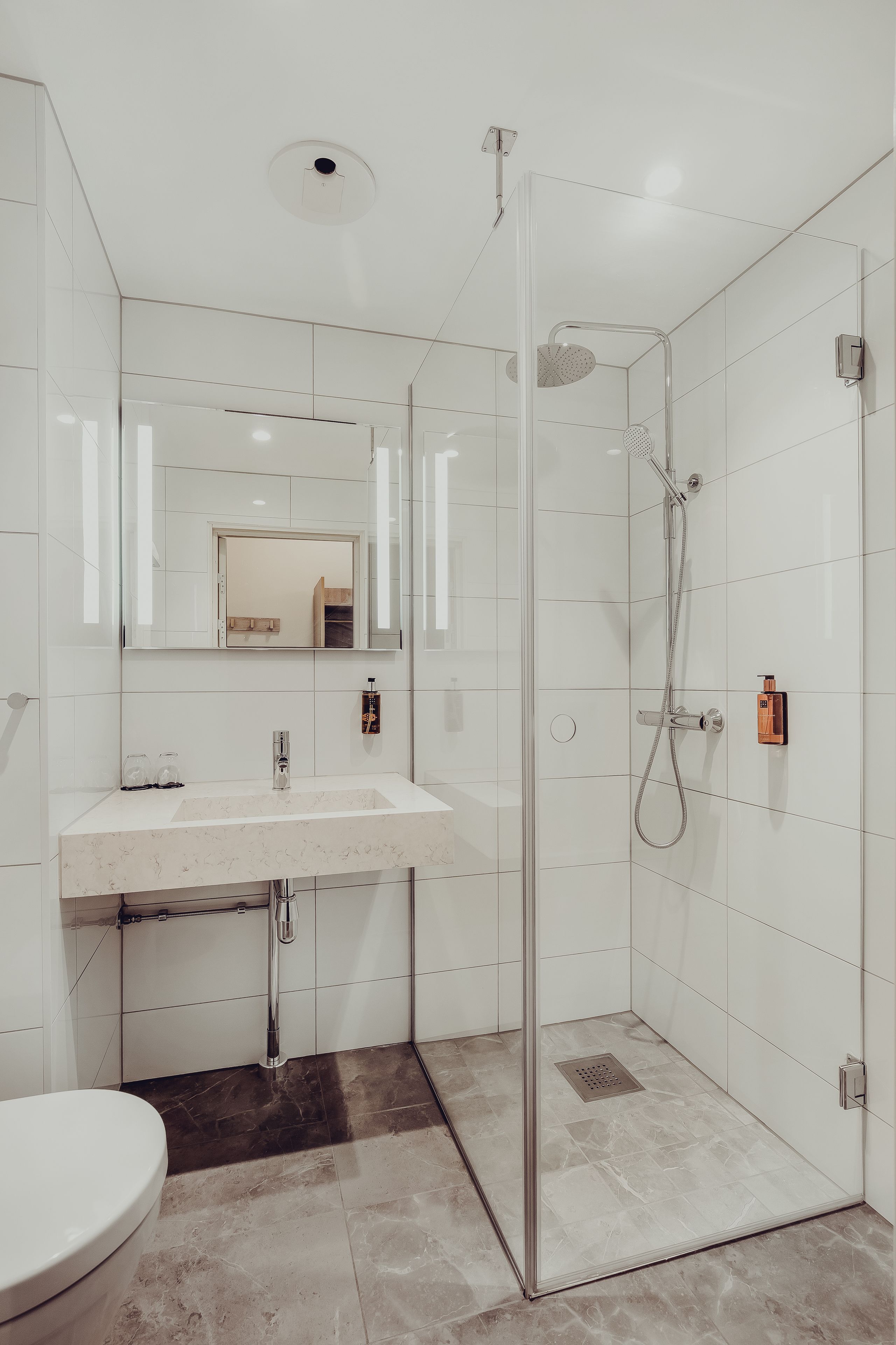 Un baño moderno con cabina de ducha de vidrio, un lavamanos blanco y un espejo sobre él.