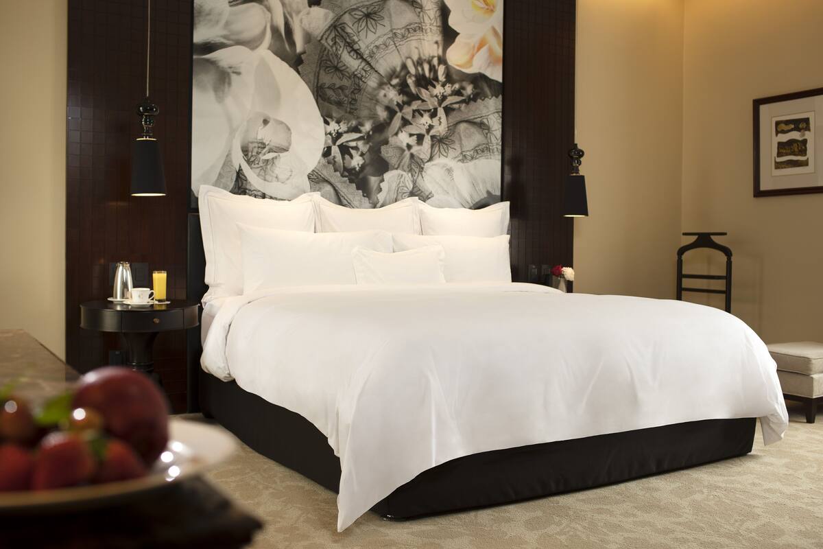 Ein ordentlich bezogenes Bett mit weißen Leinen und einem dunklen Kopfteil in einem Hotelzimmer.